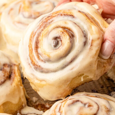 A cinnamon roll being picked up out of a pan of cinnamon rolls.