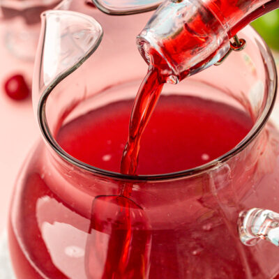 Cherry simple syrup being poured into a pitcher.