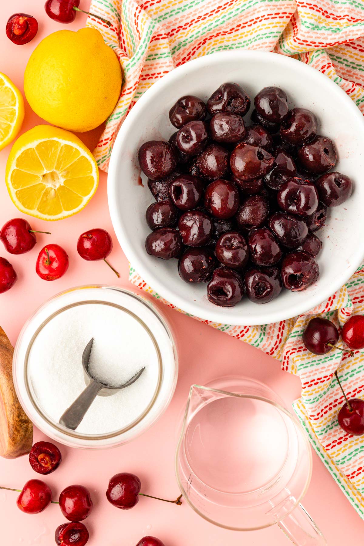 Overhead photo of ingredients to make cherry simple syrup: cherries, lemons, water, and sugar.