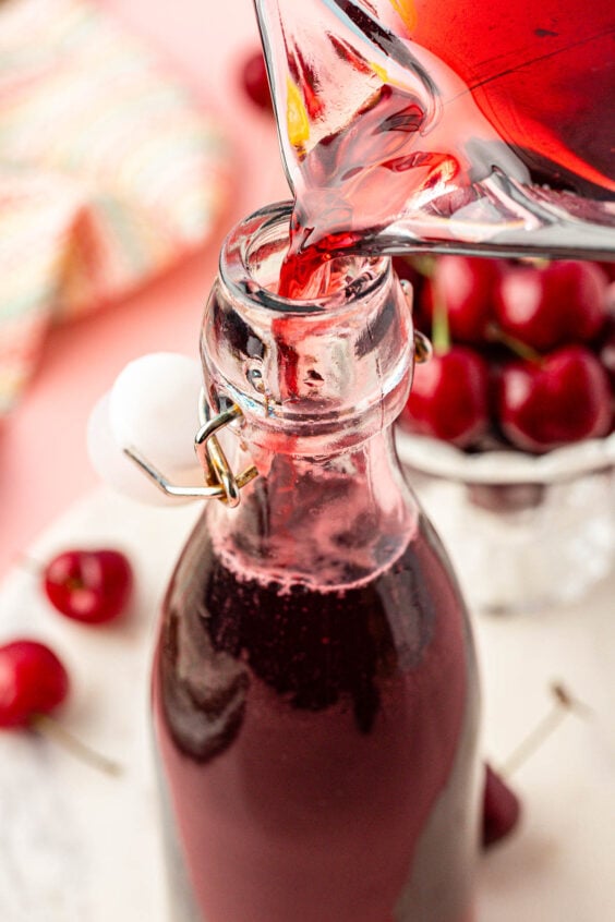 Cherry simple syrup being poured into a glass bottle.