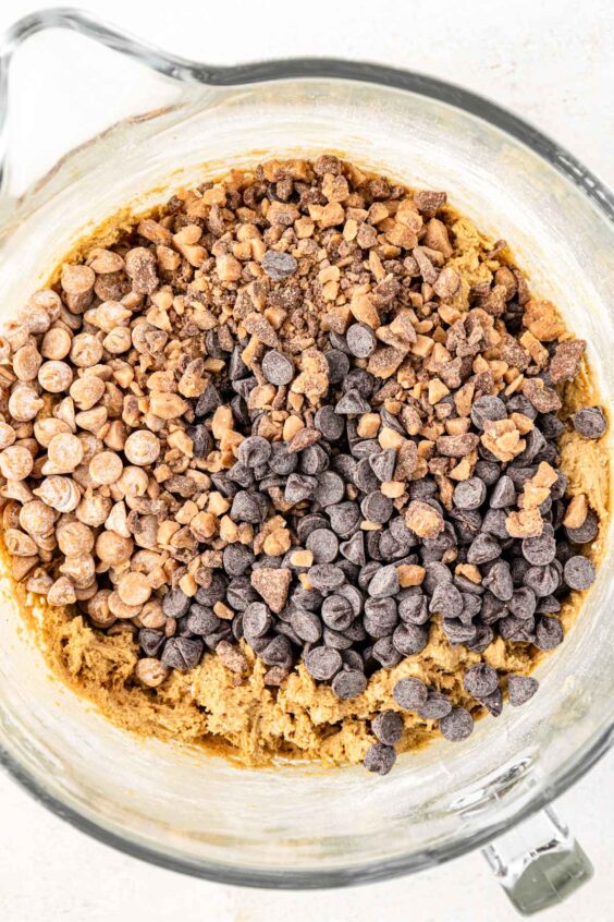 Chocolate chips, peanut butter chips, and toffee bits being added to cookie dough.