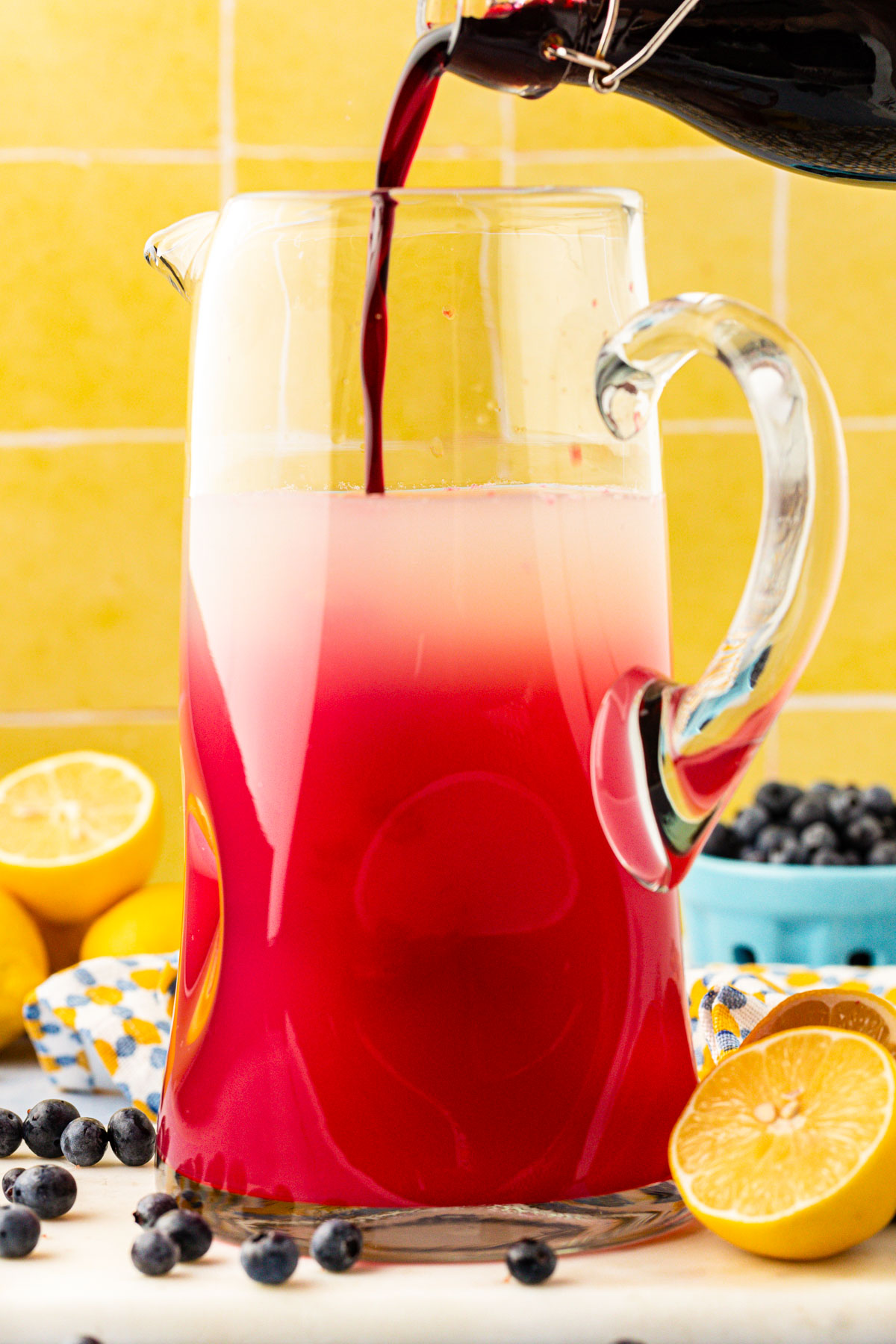 Blueberry lemonade being prepared in a large glass pitcher.