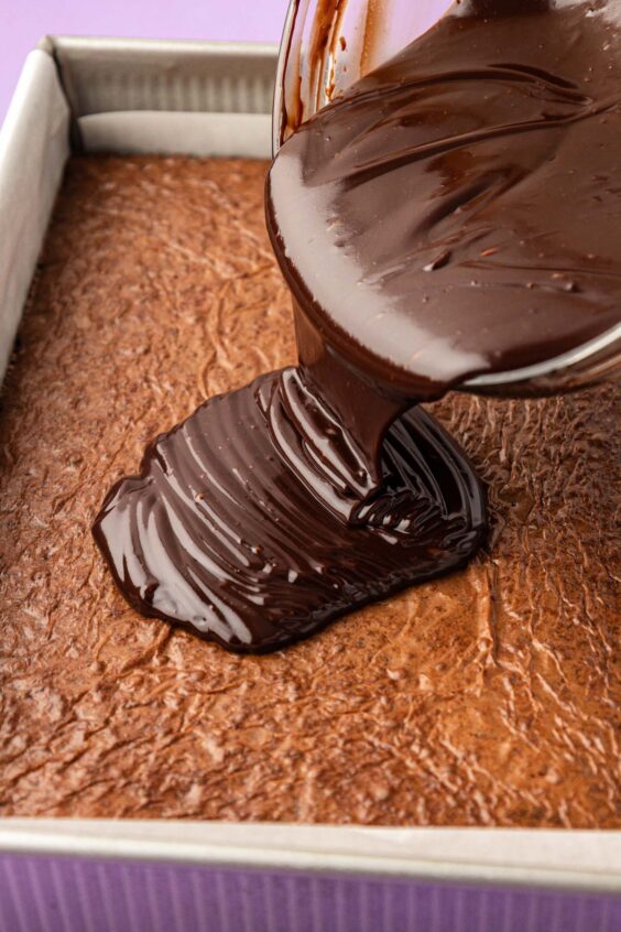 Ganache being poured over the top of baked brownies.