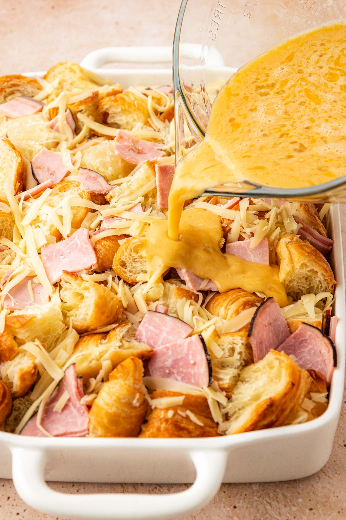 Egg mixture being poured over ham and cheese breakfast casserole before baking.