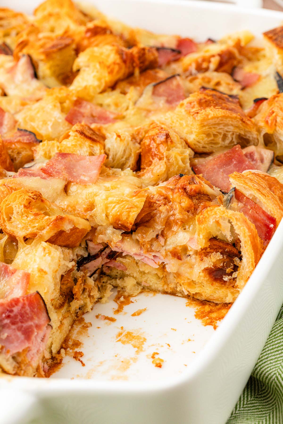 Close up of a croissant breakfast casserole in a white baking dish.