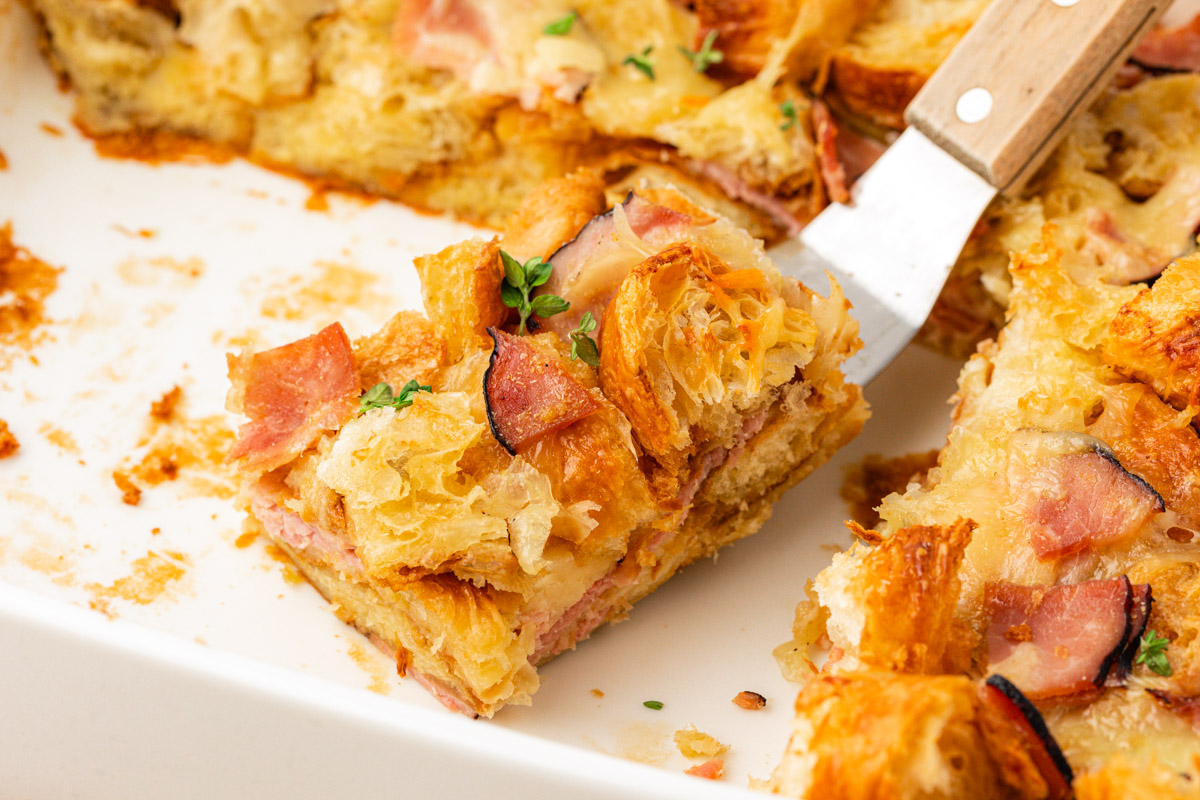 A slice of ham and cheese croissant breakfast casserole on a spatula.