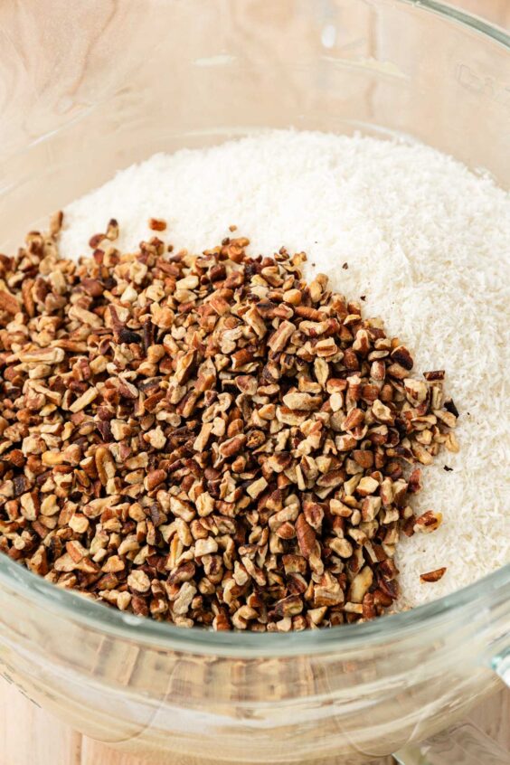 Pecans and coconut being added to cake batter in a glass bowl.