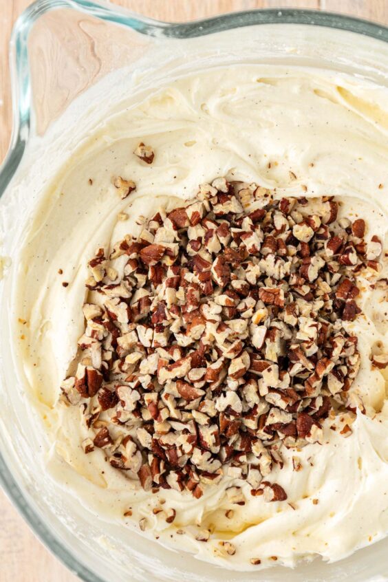 Pecan chips being added to a bowl of cream cheese frosting.