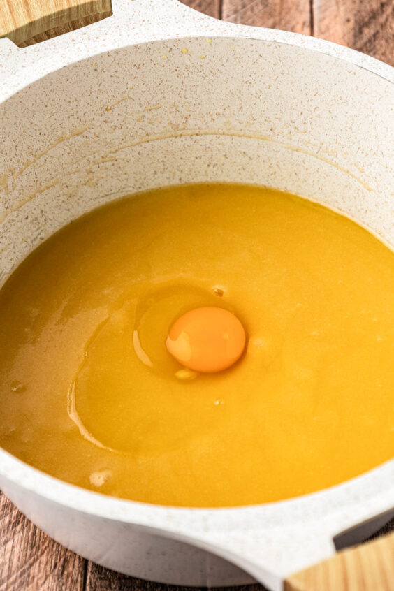 Egg being added to a pot with other ingredients to make brownie batter.