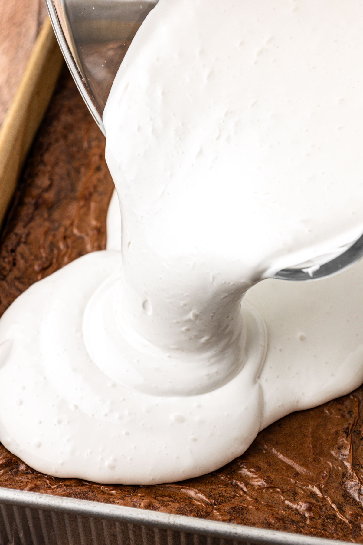 Marshmallow cream being poured over the top of the brownies.