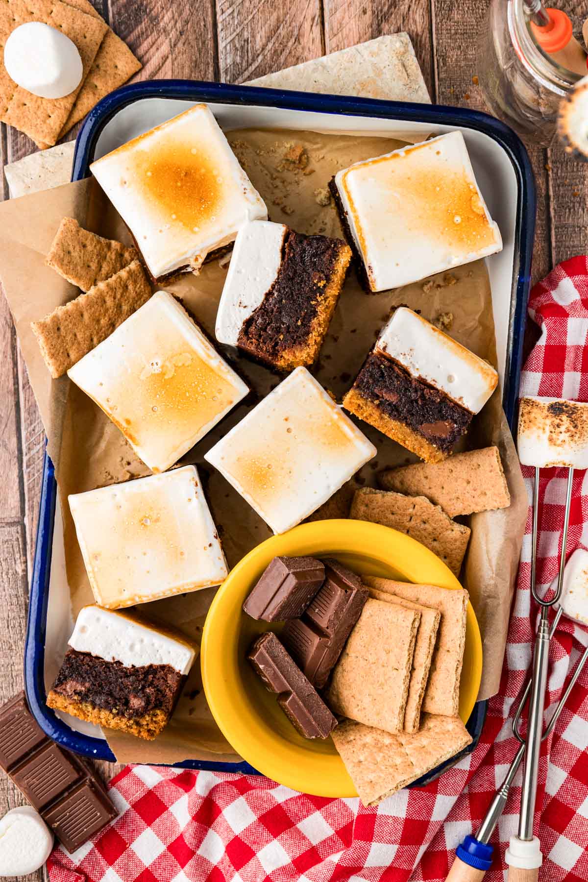 Overhead photo of S'mores Brownie squares in a enamel pan on a wooden table.