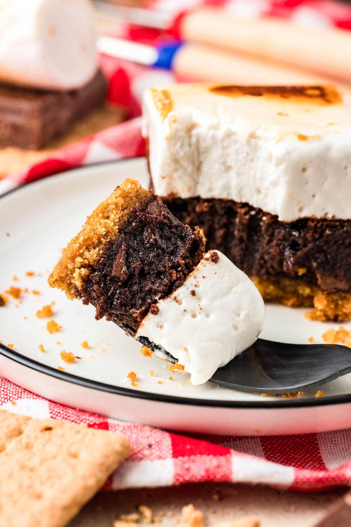 A fork with a bite of s'mores brownie on a white plate.