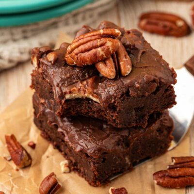 A stack of two iced brownies on a piece of parchment.