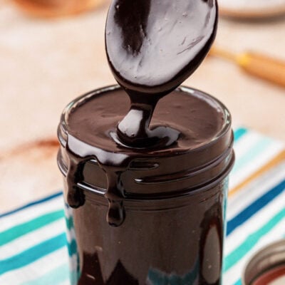 Close up of a spoon scooping hot fudge from a jar.