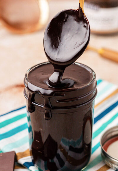 Close up of a spoon scooping hot fudge from a jar.