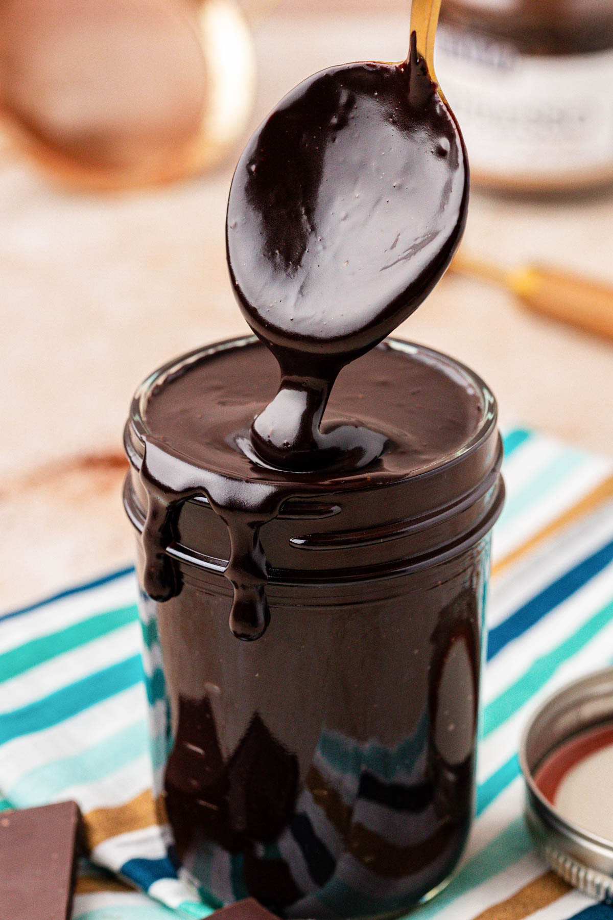 Close up of a spoon scooping hot fudge from a jar. 