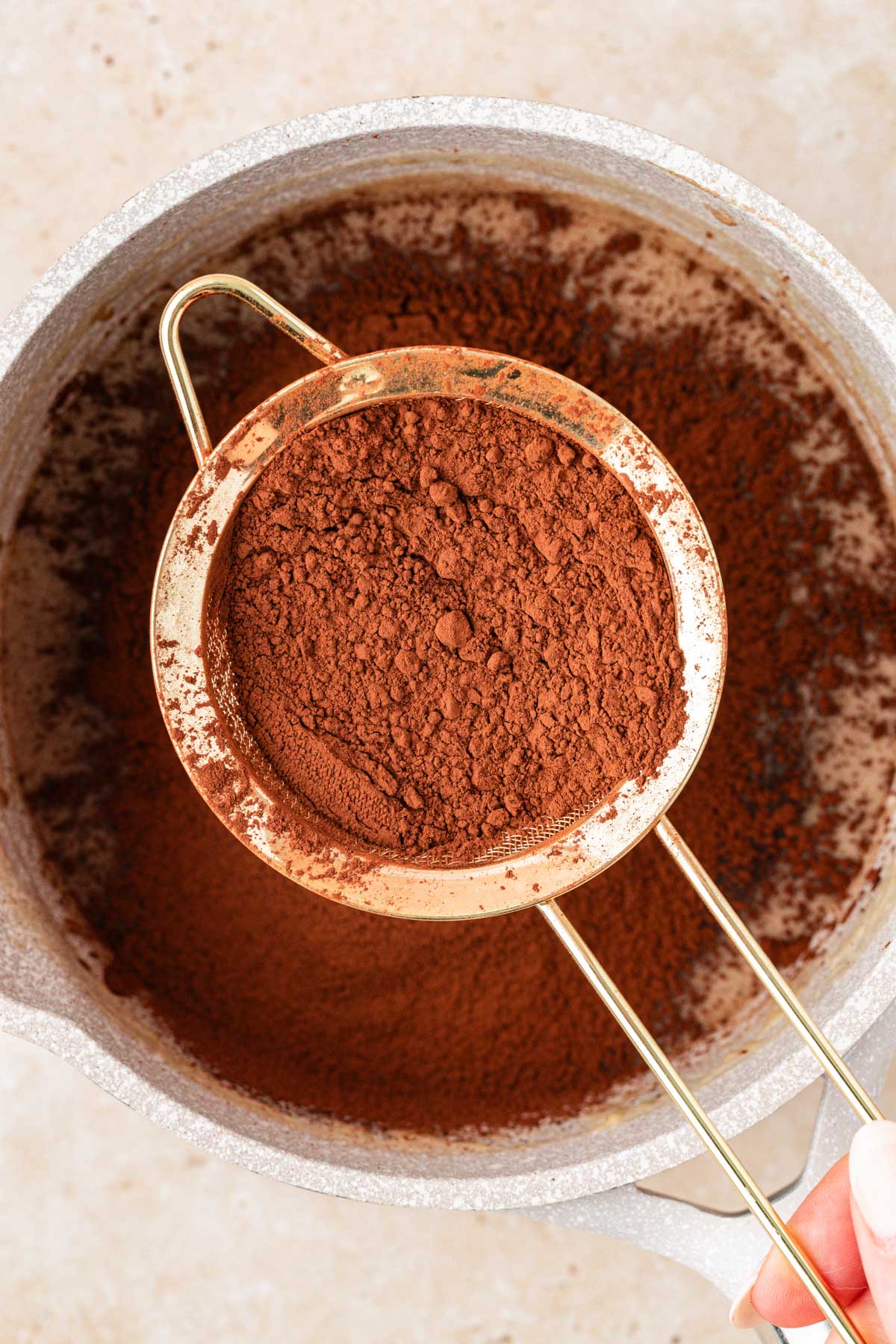 Cocoa powder being sifted into a pot to make hot fudge.