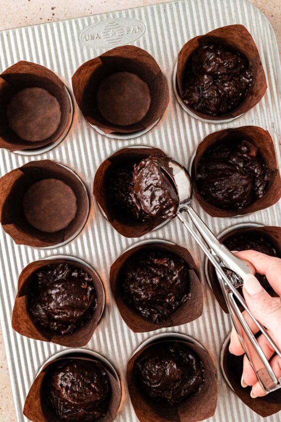 Muffin liners being filled with chocolate muffin batter.