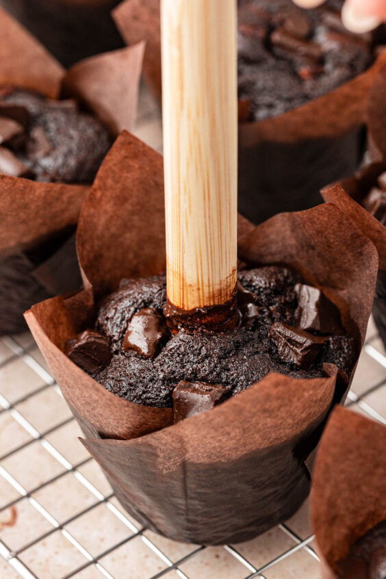 A wooden dowel poking a hole in a chocolate muffin.