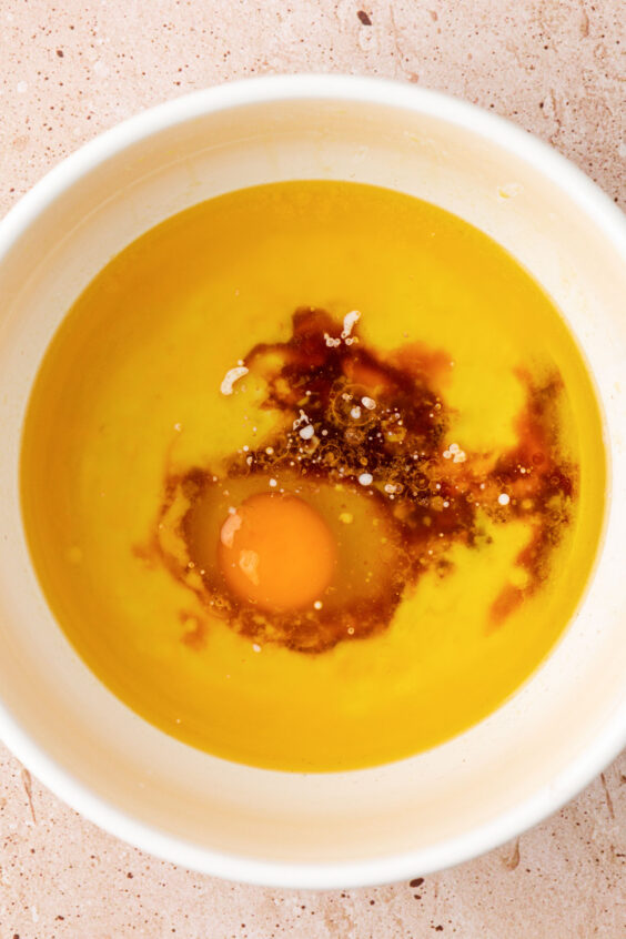 Egg being added to a bowl with melted butter and oil.