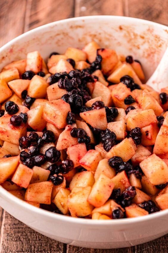 Blueberries and apples being stirred in a bowl with ingredients to make apple crisp.