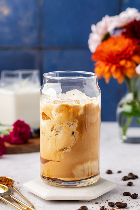 Ice and coffee foam in a glass on a white coaster on a table.