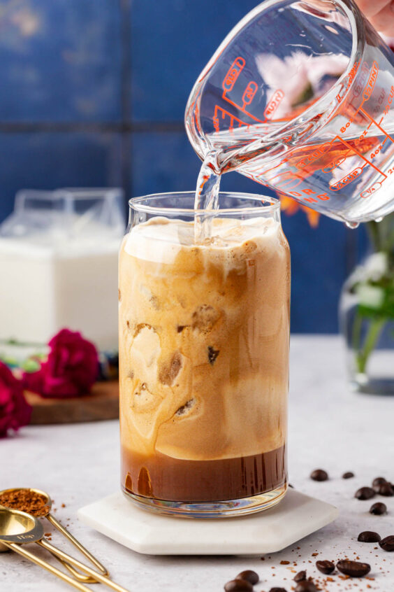 Water being poured into a glass with coffee foam to make a greek frappe drink.