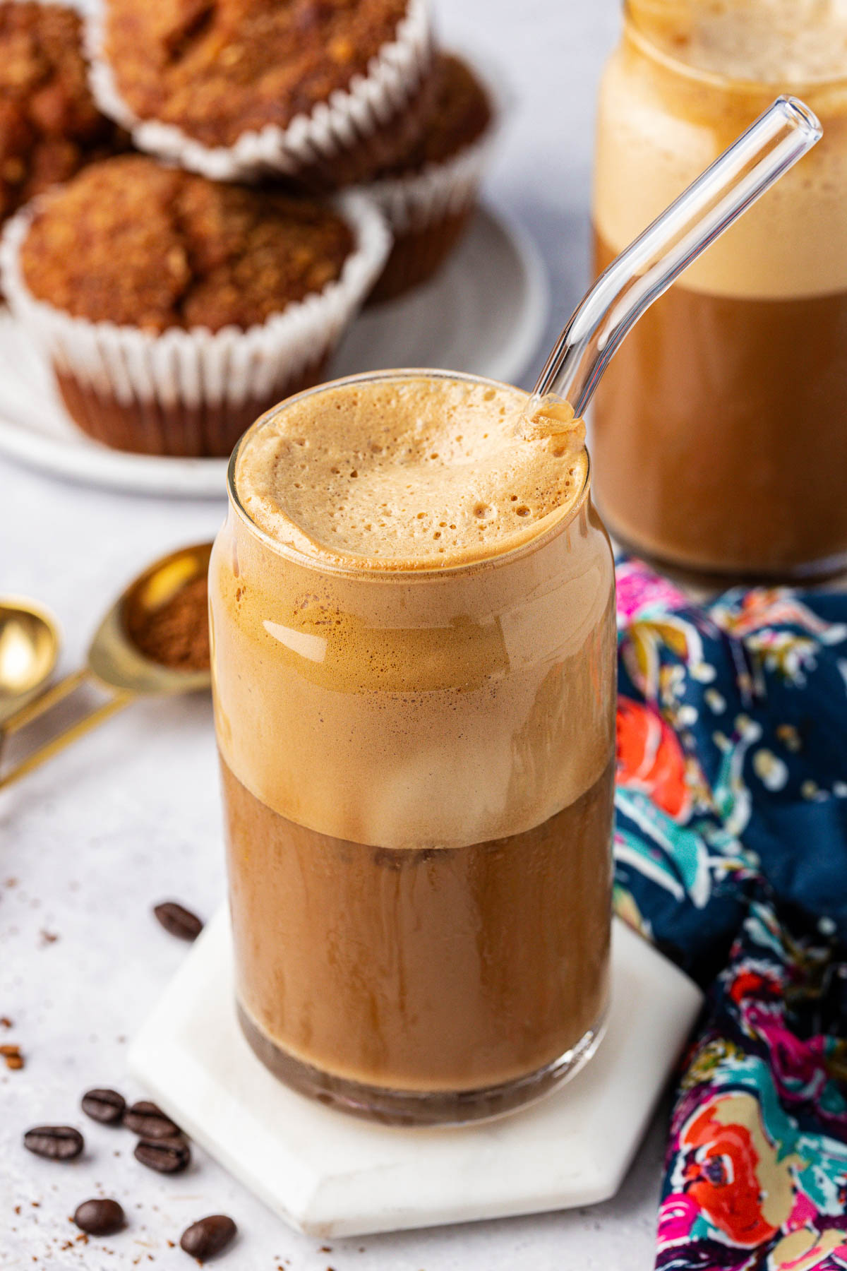 A glass with a Greek Frappe coffee prepared in it on a white coaster on a table.