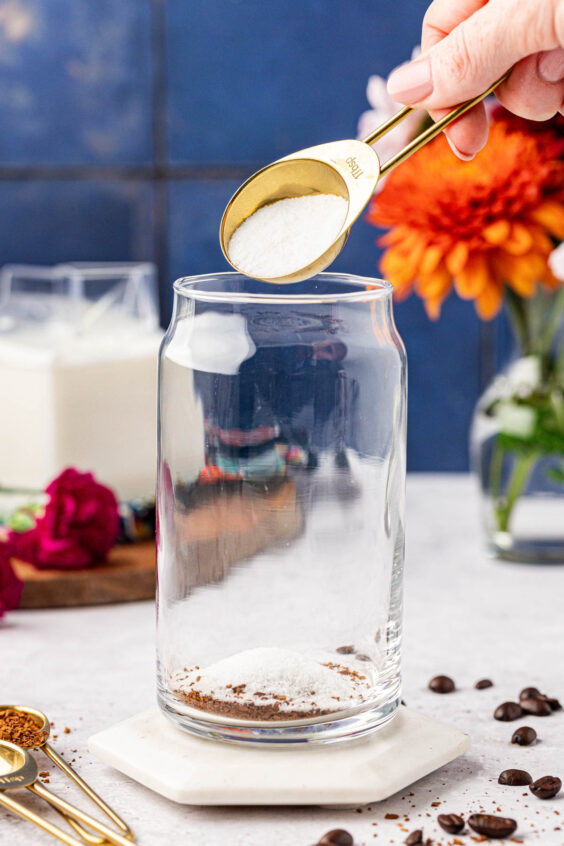 Sugar being added to a glass with instant coffee granules.