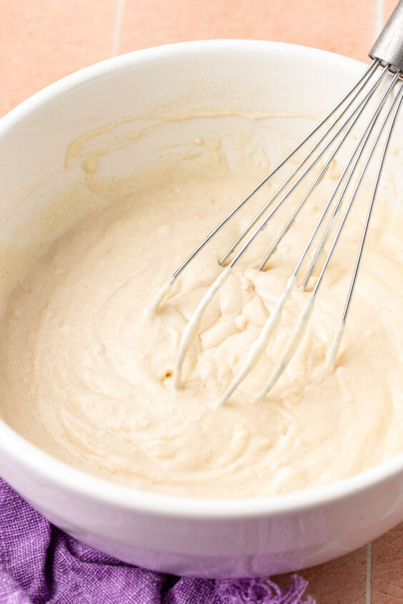 Pancake batter being whisked together in a white bowl.