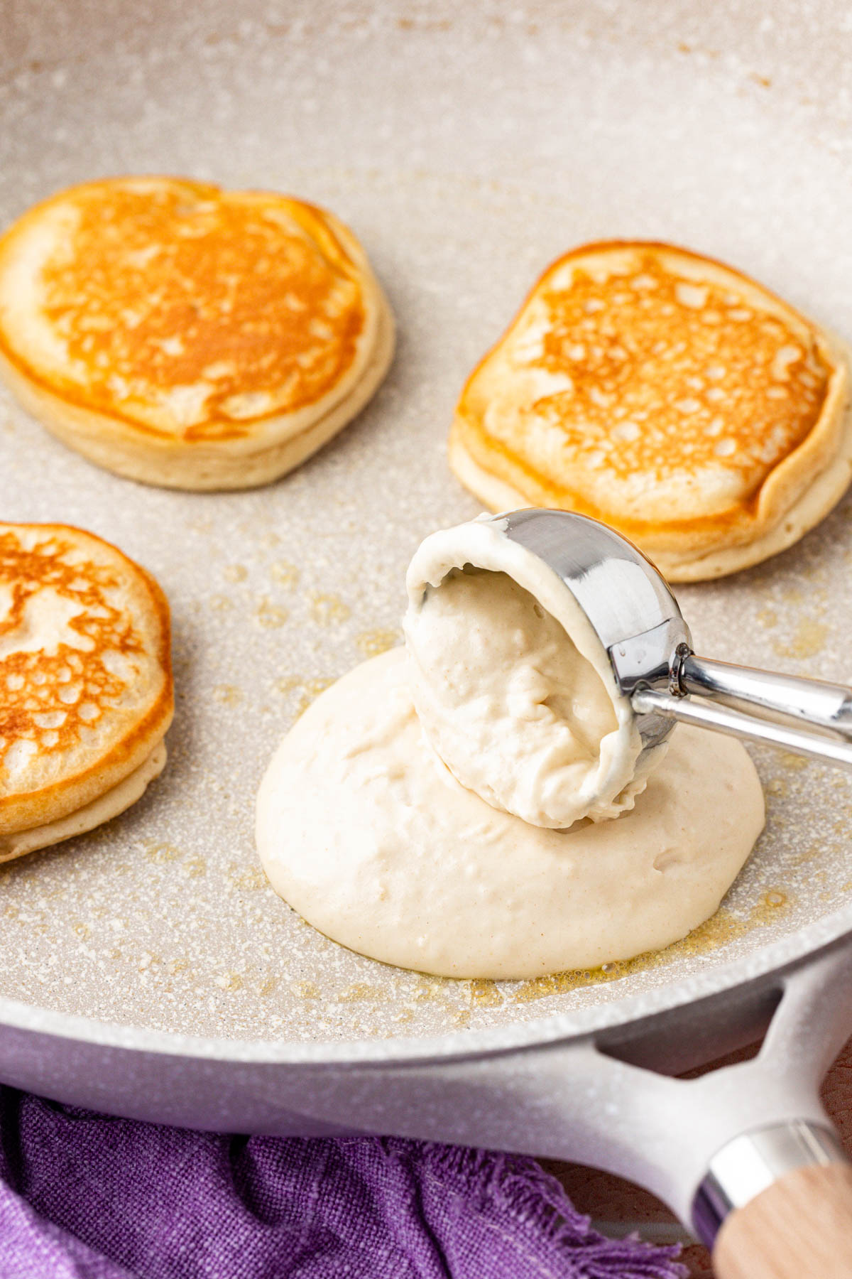 A scoop dropping pancakes batter on a skillet.