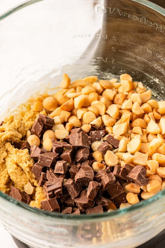 Chocolate chunks and macadamia nuts being added to a mixing bowl with cookie dough.