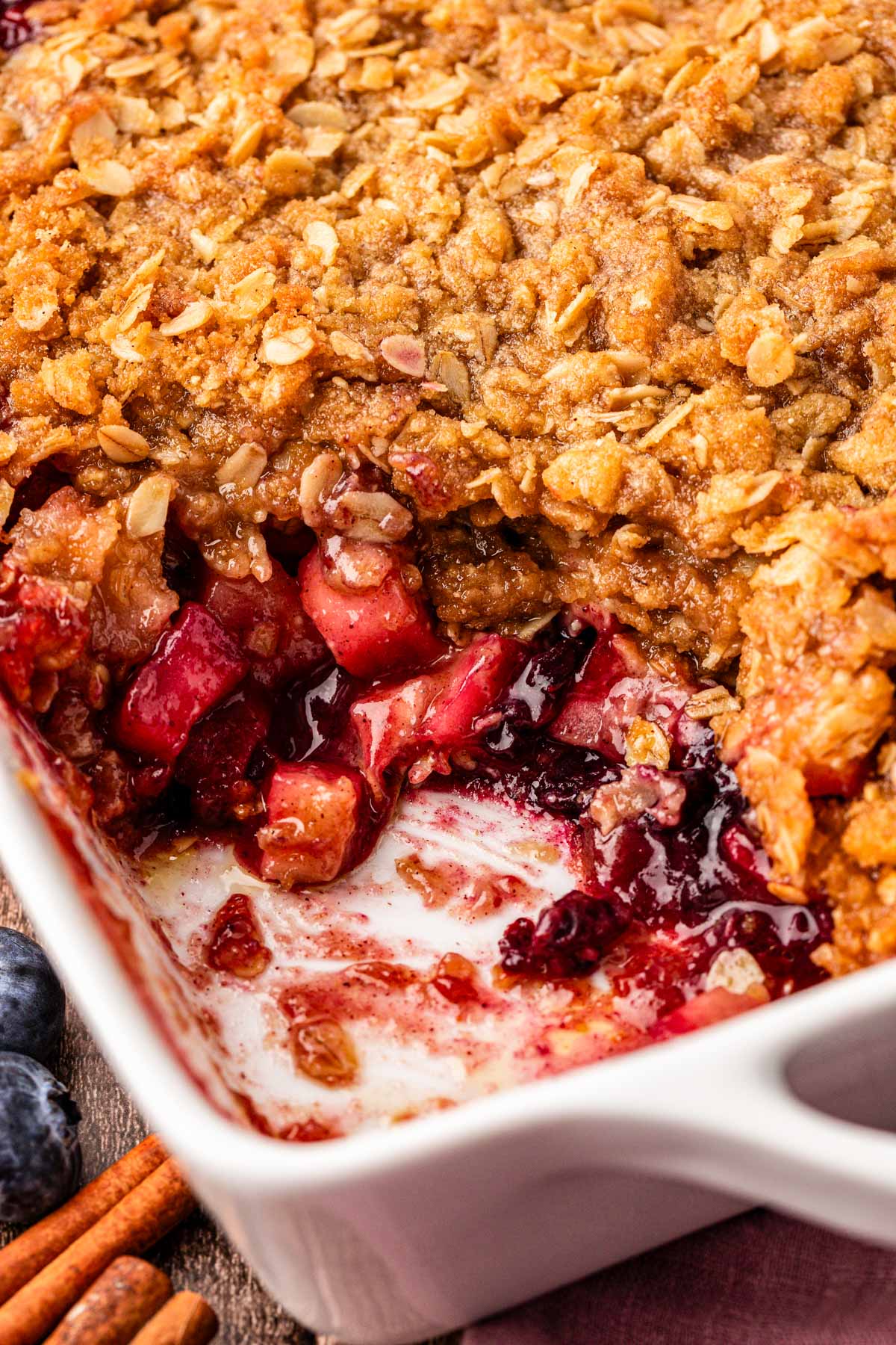 Close up photo of apple blueberry crisp in a dish missing a scoop.