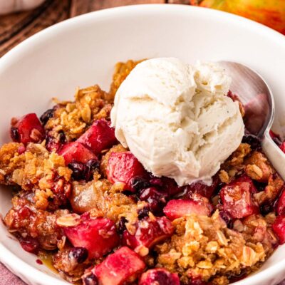 Close up of blueberry apple crisp in a white bowl topped with vanilla ice cream.