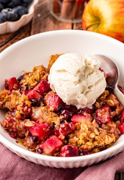 Close up of blueberry apple crisp in a white bowl topped with vanilla ice cream.