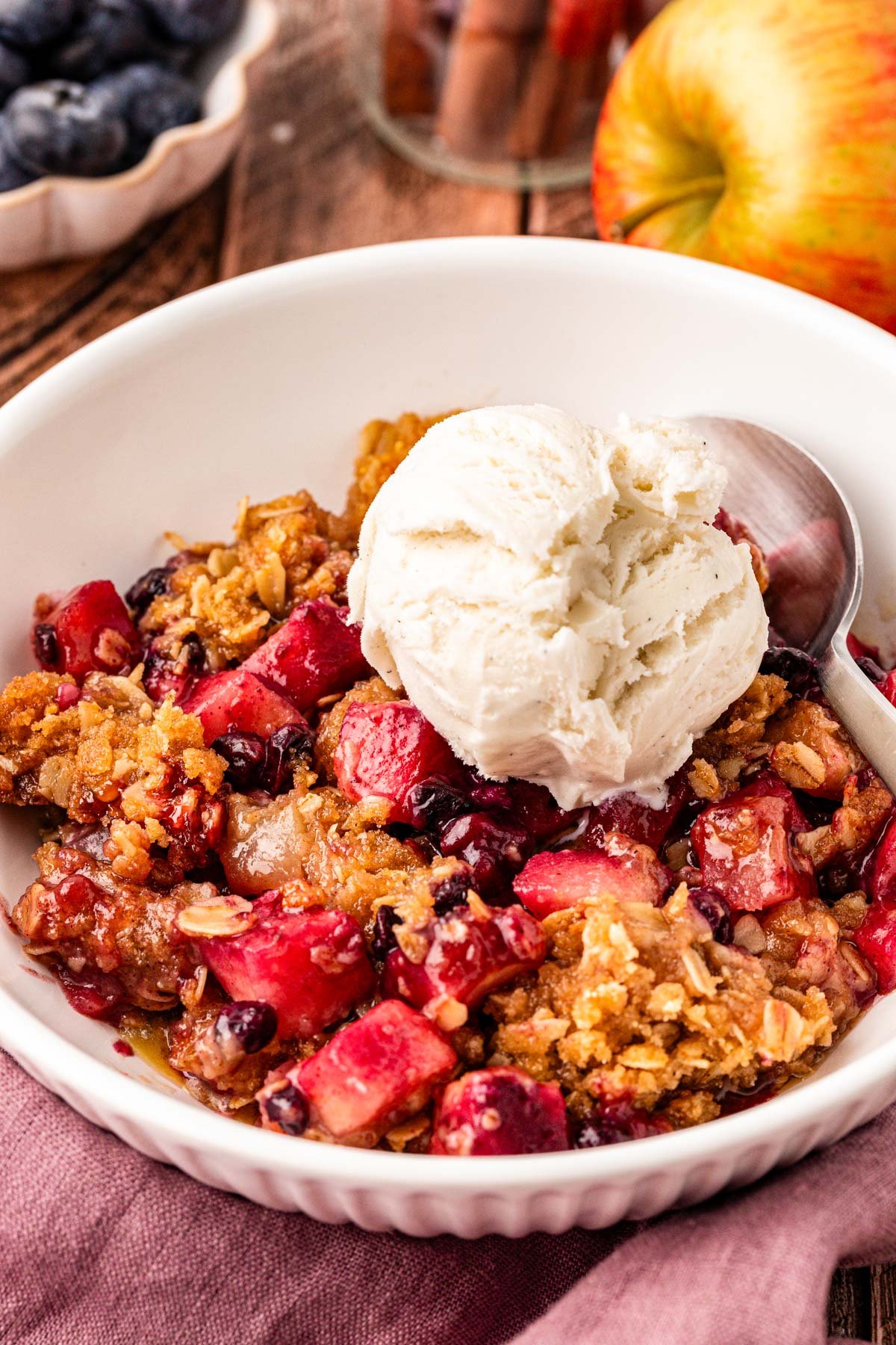 Close up of blueberry apple crisp in a white bowl topped with vanilla ice cream.