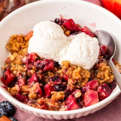 Close up of a blueberry apple crisp in a white bowl with vanilla ice cream.