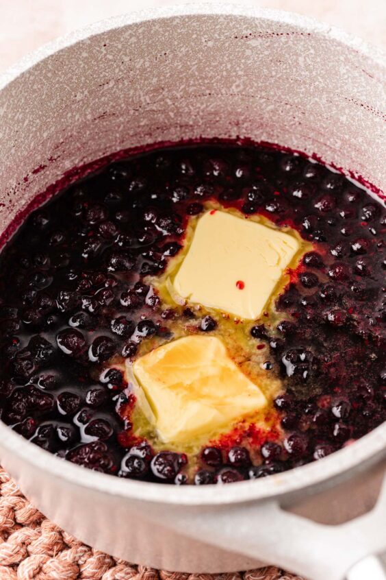 Butter being added to a pot of mixed berries that have been simmering.