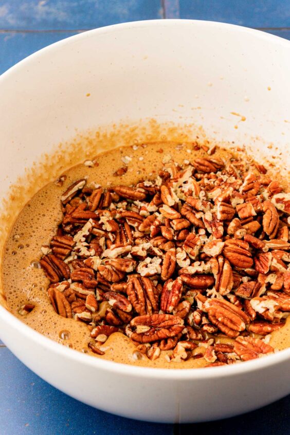 Pecan halves being added to a bowl with egg.