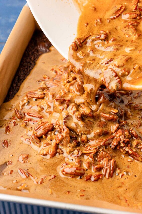 Pecan pie mixture being poured over brownies.