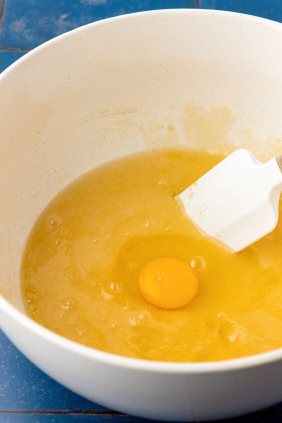 Egg being added to a butter and sugar mixture in a pot.