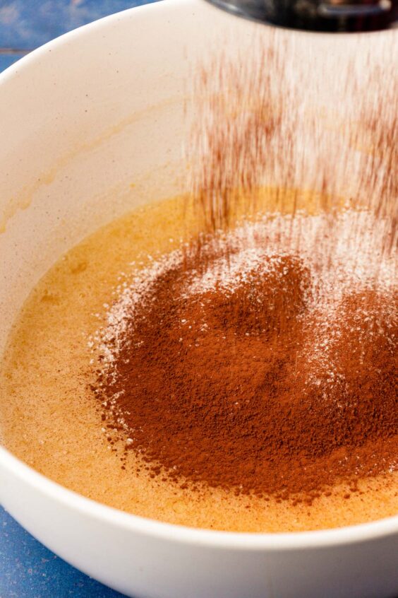 Cocoa and flour being sifted into a butter and sugar mixture.