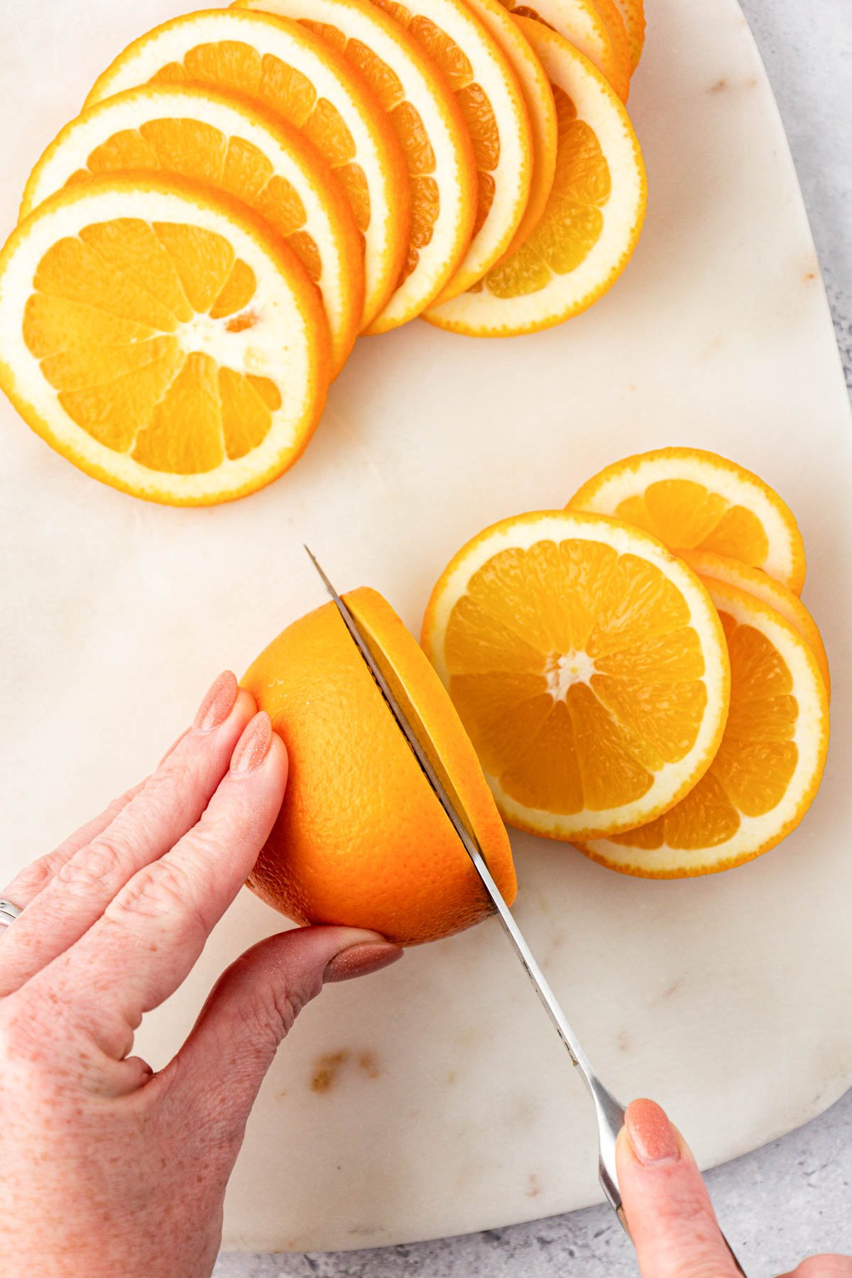 A woman's hand cutting navel oranges into slices.