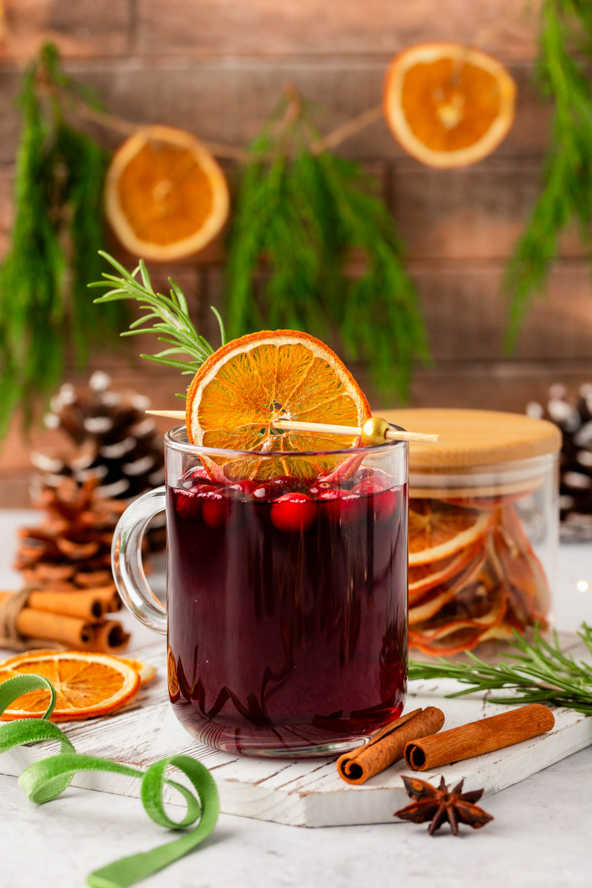 A red drink in a mug with cinnamon and dried oranges around it.