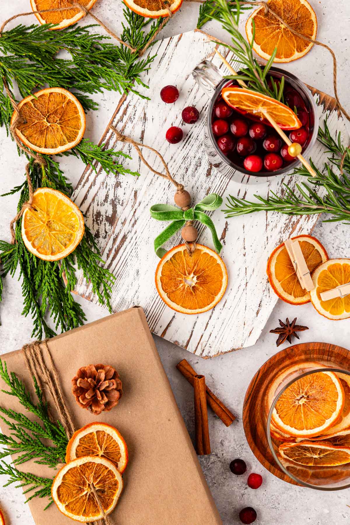 Overhead of dried orange slices and holiday decor and garnishes on a white table.