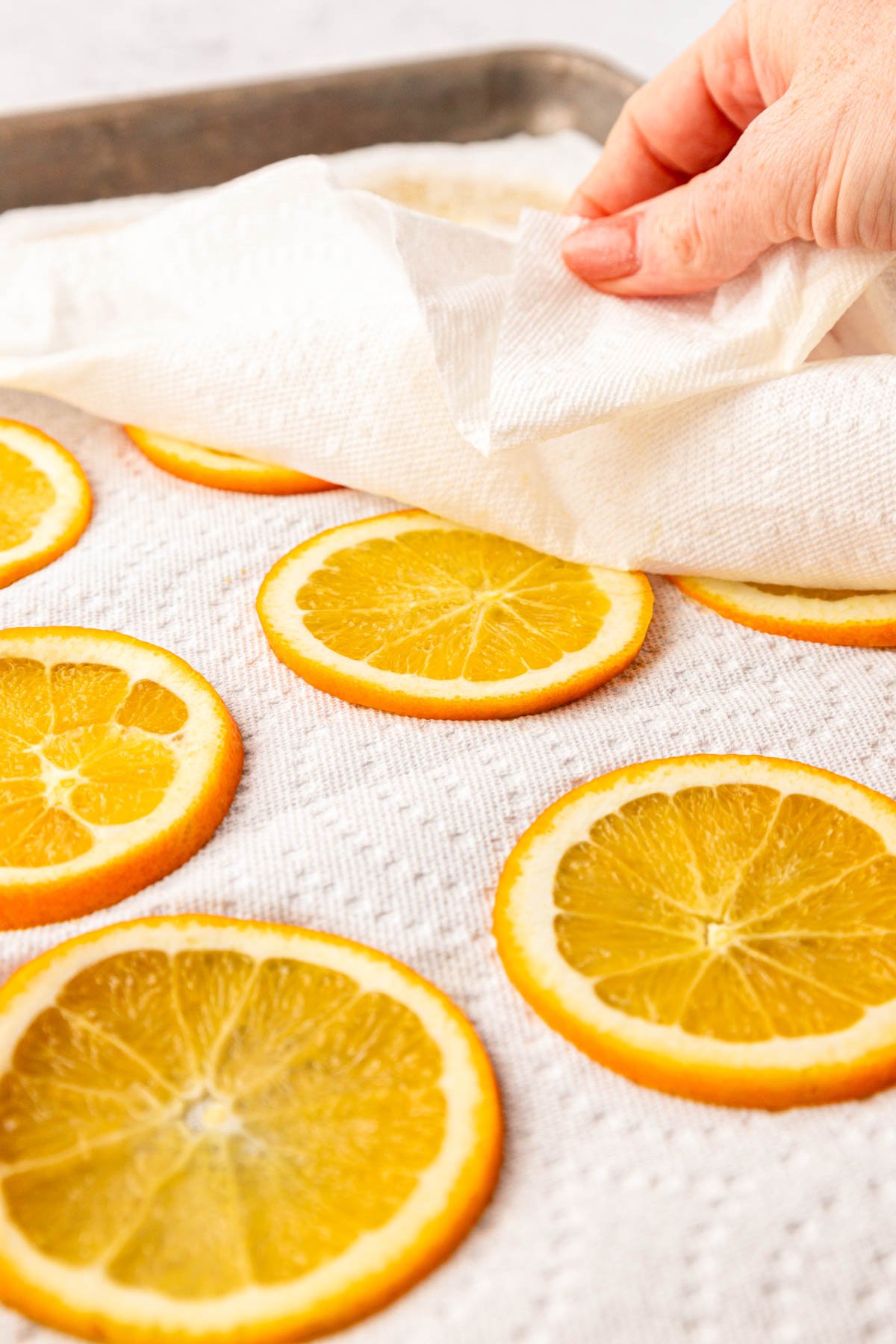 A woman's hand patting down orange slices with a paper towel.