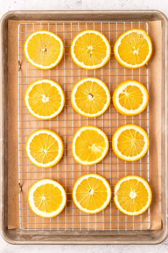 Orange slices arranges on a wire rack on a baking sheet to dry them out.