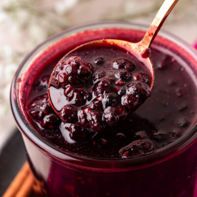 Close up of a jar of berry compote with a spoon lifting some out.