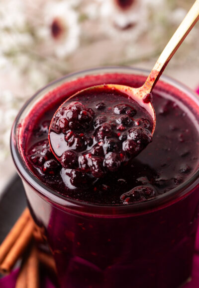 Close up of a jar of berry compote with a spoon lifting some out.