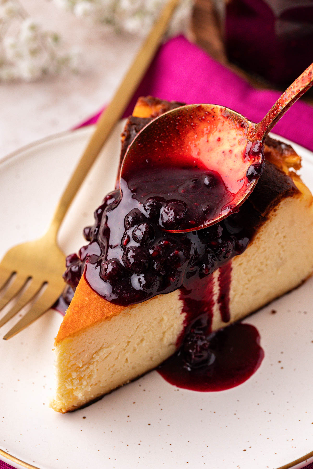 Berry compote being spooned over a slice of cheesecake.